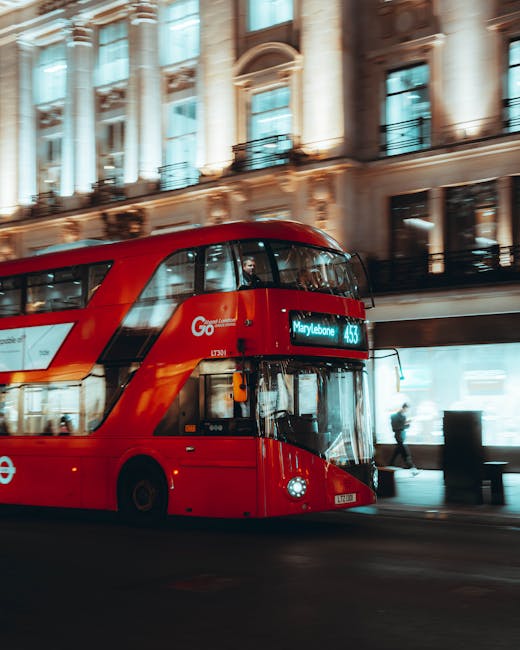 A red double-decker bus traveling along a street near a historic building with ornate architecture, tall windows, and decorative columns, illuminated by streetlights and passing traffic, capturing a typical scene of urban transportation around Marylebone. The bus displays its route to Marylebone on the front electronic sign, indicating it is part of the local transit service. This image may relate to house removals and moving logistics in the Marylebone area, such as transporting furniture or packing materials to or from a home relocation. The scene shows the busy environment often involved in moving services provided by Man with Van Marylebone, highlighting the transportation component of home removals in London.